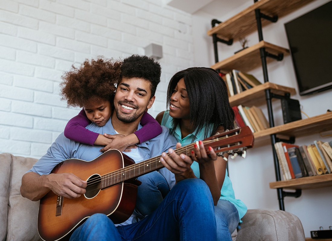Personal Insurance - Young Family Sitting Together as the Father Plays a Guitar